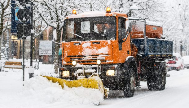 A snow plow at work during snowfall on whitewashed streets in the city