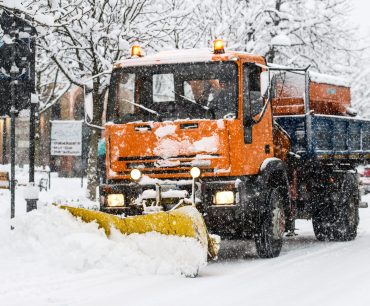 A snow plow at work during snowfall on whitewashed streets in the city