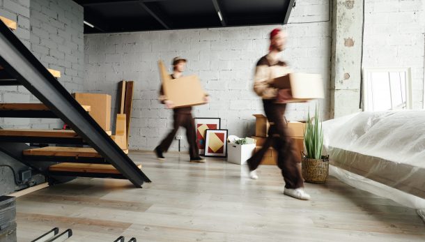 Blurred motion of loaders in workwear carrying packed cardboard boxes while helping to deliver packages to new flat, house or studio