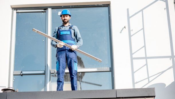 Portraiit of a builder in uniform standing with level on the balcony of a new house on the construction site
