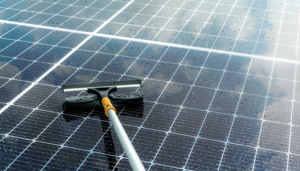 Cleaning solar panel with microfiber mop on wet roof. Solar panel or photovoltaic module maintenance service. Sustainable resource. Solar power. Green energy. Sustainable development technology.