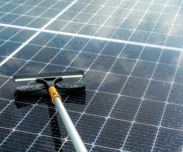Cleaning solar panel with microfiber mop on wet roof. Solar panel or photovoltaic module maintenance service. Sustainable resource. Solar power. Green energy. Sustainable development technology.