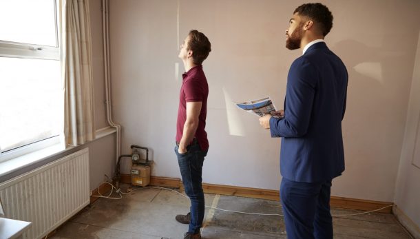 Male First Time Buyer Looking Around House For Renovation With Realtor